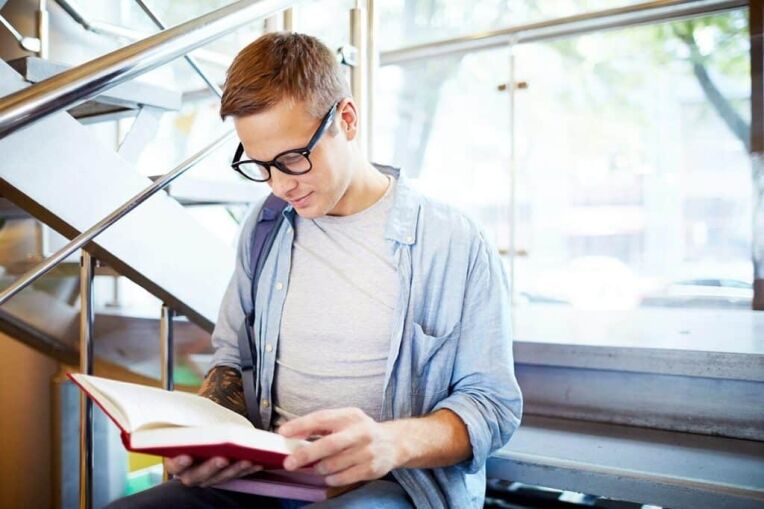 A man with glasses reads a book discussing strategies for managing college alongside mental health outpatient care