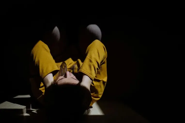 A woman in a yellow outfit sits on the floor, reflecting on trauma triggers and their management.